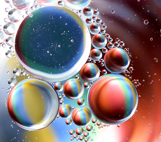 Image shows oil droplets floating in water. The oil droplets act like prisms that bend the light into all the colors of the rainbow.