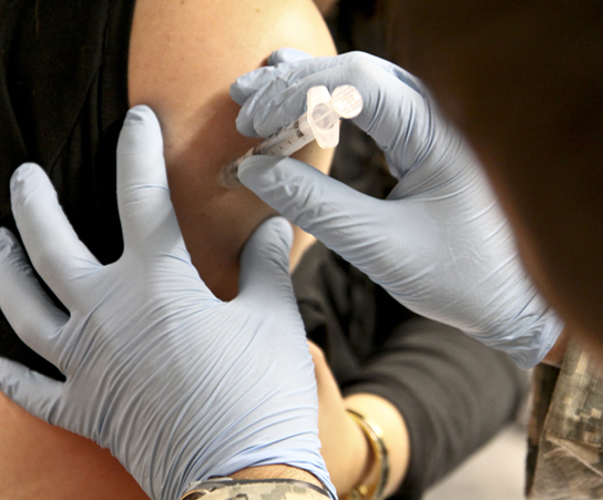 The photo shows a person receiving an injection in the arm.