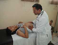 A pregnant woman is lying on a table being examined by a doctor. The doctor's hands are on her belly.