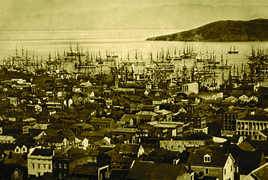 A photograph shows an aerial view of the port of San Francisco. The streets are crowded with houses, and the water teems with ships.