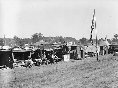 A photograph shows a row of tents with several veterans seated outside. An American flag is raised in the middle of the camp.