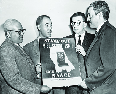 A photograph shows Henry L. Moon, Roy Wilkins, Herbert Hill, and Thurgood Marshall holding up a poster that reads “Stamp Out Mississippi-ism! Join NAACP.” In the middle of the poster, a graphic shows the state of Mississippi with a tombstone in the center. The tombstone displays the names of four African Americans murdered in Mississippi in 1955.