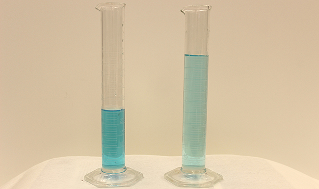 This figure shows two graduated cylinders side-by-side. The first has about half as much blue liquid as the second. The blue liquid is darker in the first cylinder than in the second.
