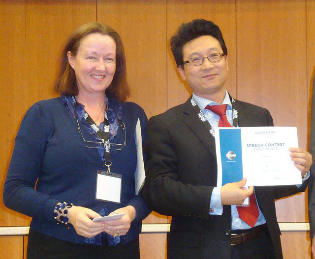 A woman and a man smiling as he holds a certificate for having won an Evaluation Contest