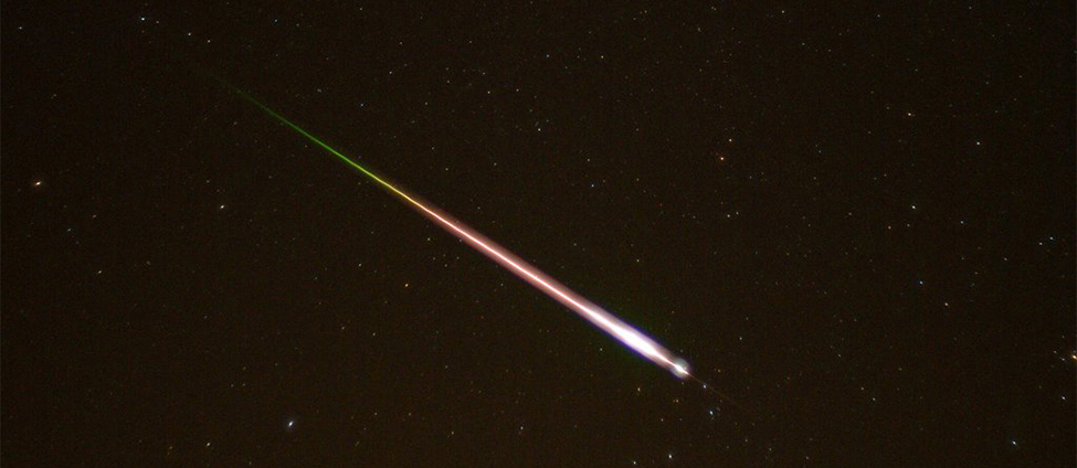 This is a photo taken of the night sky. A meteor and its tail are shown entering the earth's atmosphere.