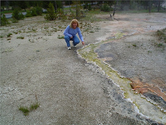 Picture of a hot spring at Yellowstone National Park with a woman next to it.