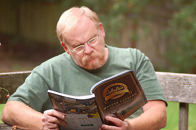An outdoorsman reading a Cabela's' catalog
