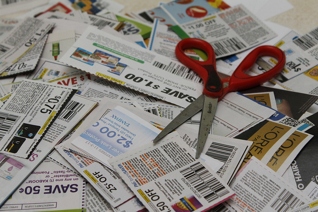 A large pile of coupons on a table with a scissors resting on top