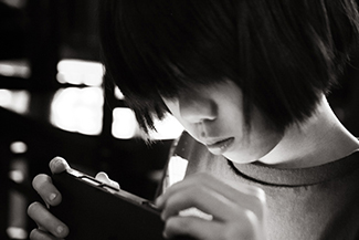 A photograph shows a young person looking at a handheld electronic device.