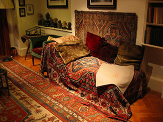 This photograph shows what Freud’s famous psychoanalytic couch looked like. The couch is draped in tapestries and pillows, and the room is decorated with sculptures, books and pictures on the wall.