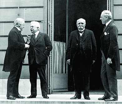 A photograph shows David Lloyd George, Vittorio Orlando, Georges Clemenceau, and Woodrow Wilson conversing outside of a building at the Paris Peace Conference.