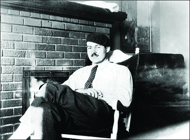 A photograph shows Ernest Hemingway reclining in a chair in front of a fireplace.