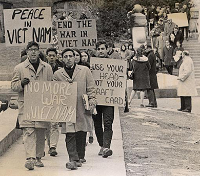 A photograph shows students protesting on the University of Madison-Wisconsin campus. They hold signs reading “No more war in Viet Nam”; “Peace in Viet Nam”; “End the war in Viet Nam”; and “Use your head—not your draft card.”
